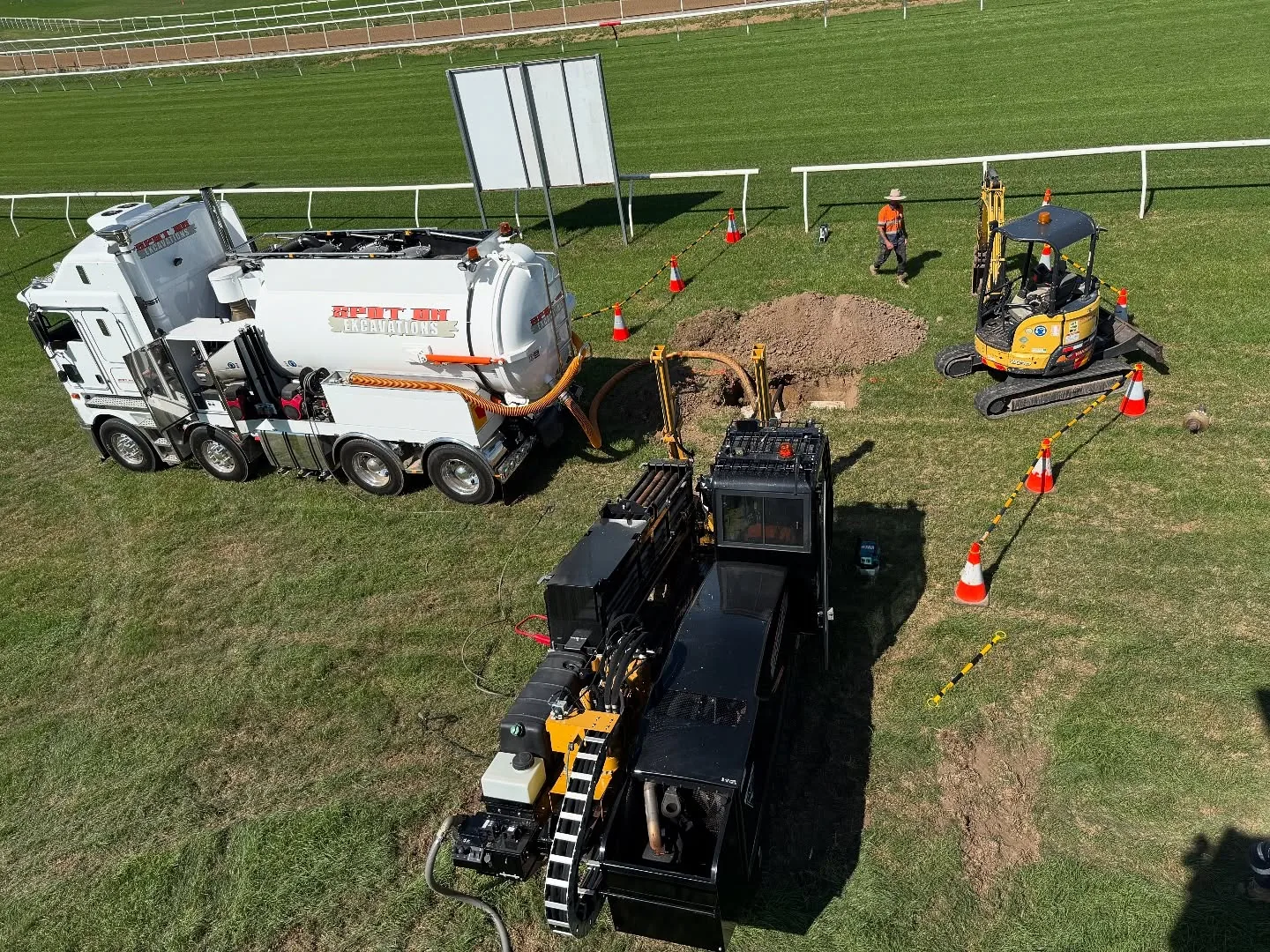Overhead view of the Spot On drill, hydrovac truck and excavator working beside the racecourse.