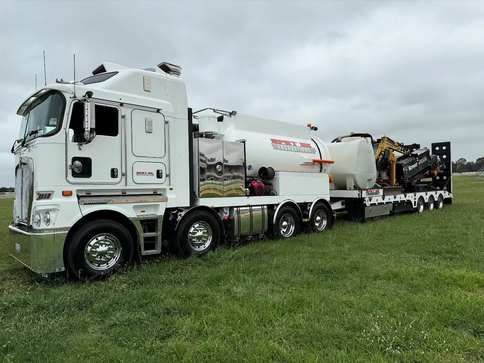 Spot On vacuum truck and drilling rig on a transport trailer beside the racecourse.